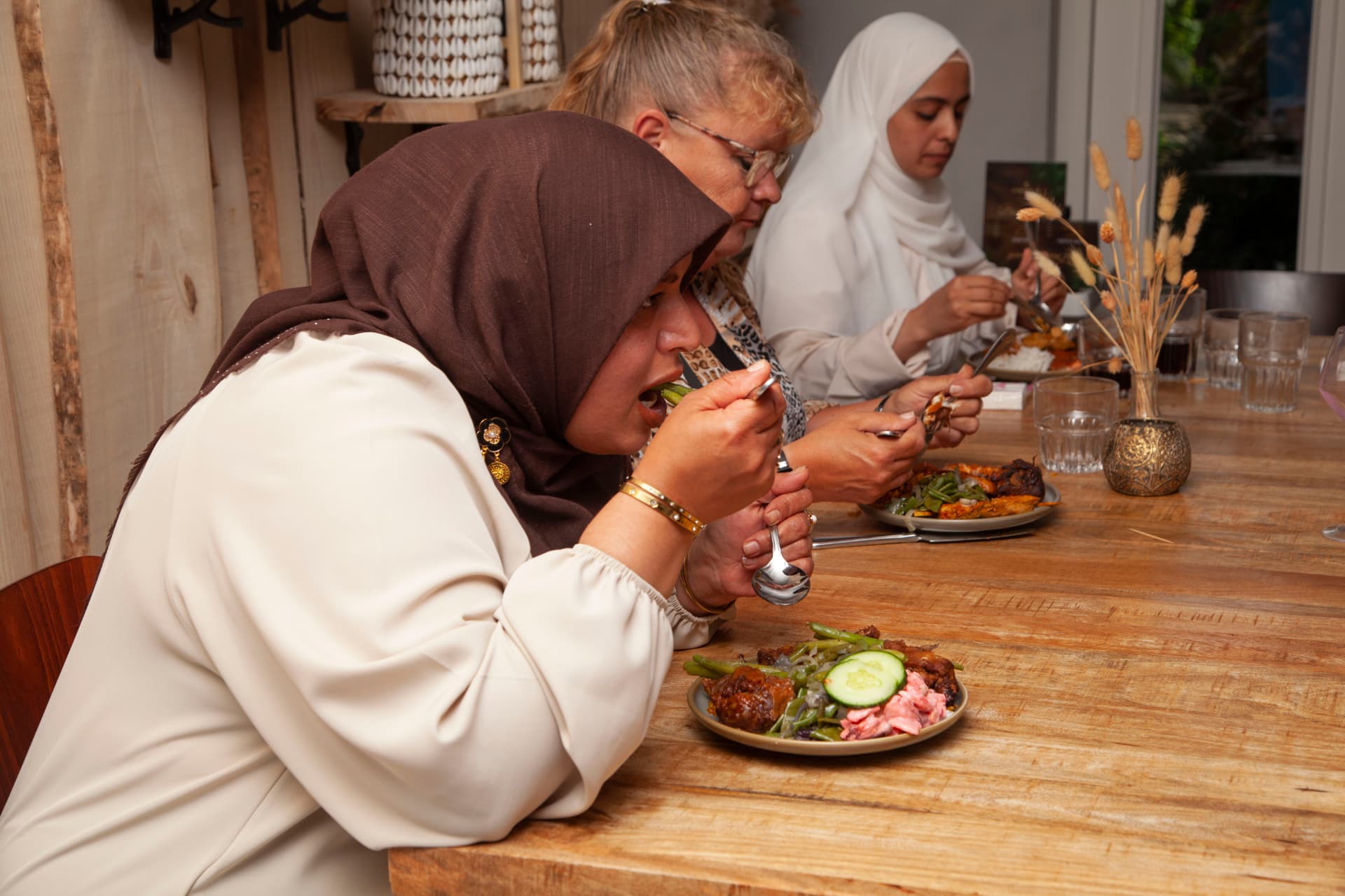 Gasten genieten samen van hun gerechten aan de lange houten tafel